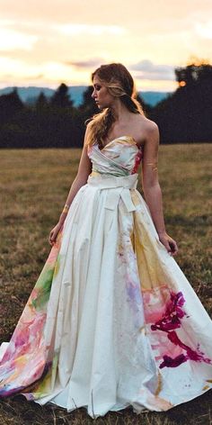 a woman standing in a field at sunset wearing a dress with flowers on the skirt