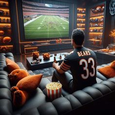 a man sitting in front of a tv watching football on the television screen while eating popcorn