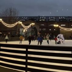 people skating on an ice rink with lights strung over the building and trees in the background