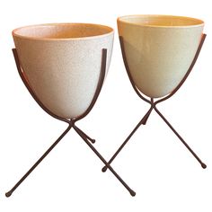 two white bowls sitting on top of metal stands with handles and legs, each holding a cup