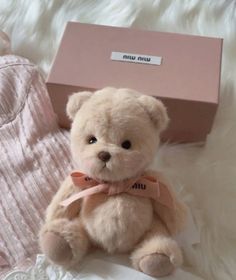 a teddy bear sitting on top of a white blanket next to a pink gift box