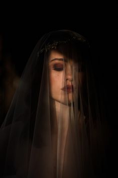 a woman wearing a veil with her eyes closed in the dark, looking at something