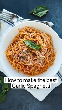 a white bowl filled with spaghetti on top of a blue table cloth next to silverware