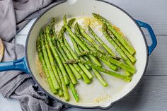 asparagus being cooked in a skillet on a white wooden table next to bread