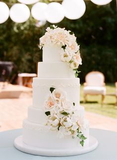 a white wedding cake with flowers on it sitting on top of a blue table cloth