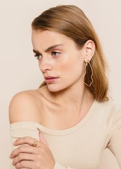 a woman wearing large gold hoop earrings and a beige off the shoulder top with long sleeves