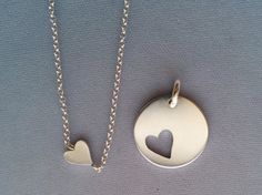 two necklaces with hearts on them sitting next to each other, one has a heart in the middle