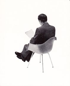 a man in a suit sitting on a chair and reading a book with his legs crossed