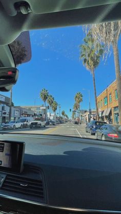 the view from inside a car looking at palm trees and cars driving down the street