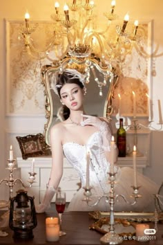 a woman in a white dress is standing near a table with candles and a chandelier