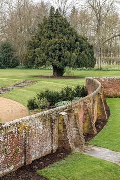 an old brick wall with grass and trees in the background