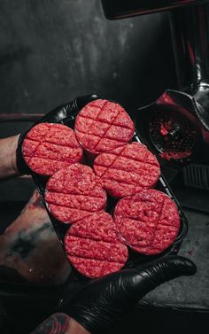 a person with tattoos holding a tray of hamburger patties in front of an oven