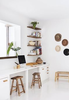 a white desk with two wooden stools in front of it and bookshelves on the wall