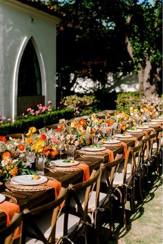 a long table is set up with orange and white place settings for an outdoor dinner