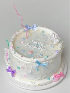 a birthday cake with white frosting and colorful bows on it's top, sitting on a plate