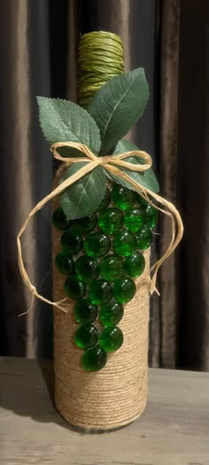 a bottle with some green glass beads and a plant in it, tied up on a table