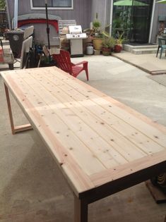 a wooden table sitting in the middle of a patio next to a red lawn chair