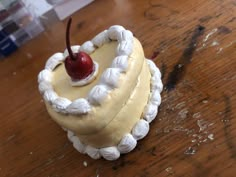 a cake with white icing and a cherry on top sitting on a wooden table