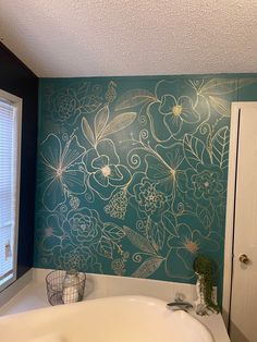 a bath tub sitting under a window next to a wall painted with flowers and leaves