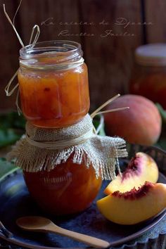 peach jam in a mason jar with spoons on a plate next to two peaches