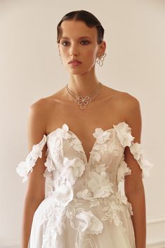 a woman in a white wedding dress with flowers on the shoulders and shoulder, wearing large hoop earrings