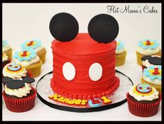 a mickey mouse cake and cupcakes on a white table with red frosting