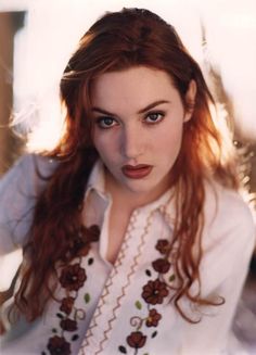 a woman with red hair and blue eyes posing for a photo in a white shirt