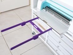 a purple and white machine sitting on top of a counter next to a shelf with drawers