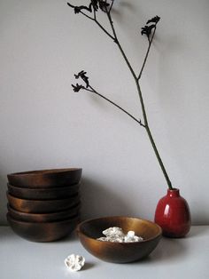 a red vase sitting next to a stack of brown bowls on top of a table