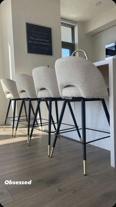 four white chairs sitting on top of a wooden floor in front of a kitchen counter