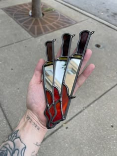 a hand holding two stained glass pieces on top of a sidewalk next to a tree