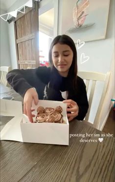 a woman sitting at a table with a box of cookies