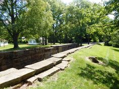 a large stone wall in the middle of a park with lots of trees and grass