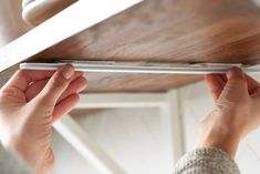 a person holding onto the edge of a wooden shelf with their hands on it and one hand reaching for something