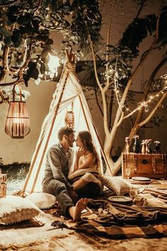 a man and woman sitting in front of a teepee with lights hanging from the ceiling