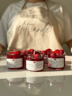 four jars of candles sitting on top of a counter next to a person wearing an apron