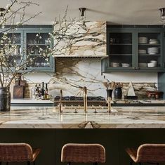 an elegant kitchen with marble counter tops and green cabinetry, along with wicker bar stools