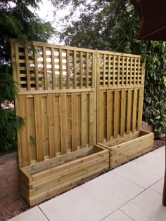 two wooden planters sitting next to each other on a patio near a fence and trees