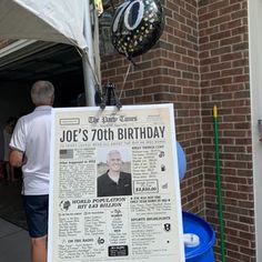 a man standing next to a blue barrel holding a sign that says joe's 70th birthday