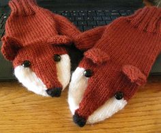 two knitted fox mittens sitting on top of a wooden table next to a laptop computer