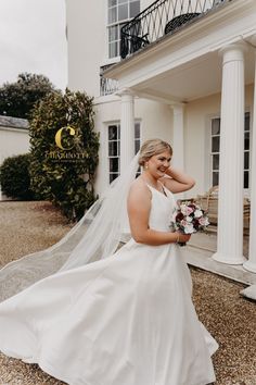 a woman in a wedding dress is posing for a photo outside her house with her veil blowing in the wind