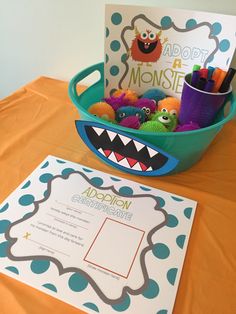 a blue bowl filled with toys on top of a table next to a sign that says adopt a monster