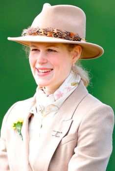 a woman wearing a tan hat and jacket smiles at the camera while standing in front of a green background