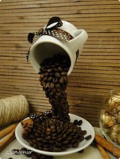 a white plate topped with lots of coffee beans next to cinnamon sticks and a vase filled with chocolates