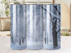 two stainless steel tumblers sitting on top of a table next to each other with trees in the background