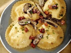 a plate filled with ravioli and mushrooms on top of a brown tablecloth covered table