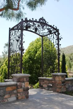 an iron gate with stone pillars in front of trees