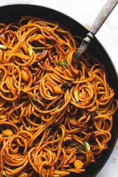 a pan filled with noodles and vegetables on top of a white countertop next to a wooden spoon