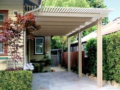 an outdoor covered patio area with plants and shrubs on either side of the house,