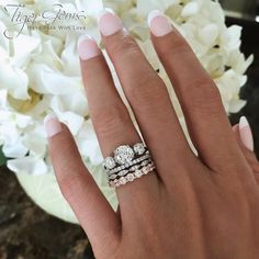 a woman's hand with three rings on it and white flowers in the background